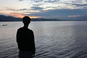 silhouet van een jong Mens staand door de meer genieten van de zonsondergang. vredig atmosfeer in natuur foto