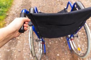 hand met lege rolstoel in ziekenhuispark wachtend op patiëntendiensten. rolstoel voor persoon met een handicap buiten geparkeerd. toegankelijk voor personen met een handicap. gezondheidszorg medisch concept. foto