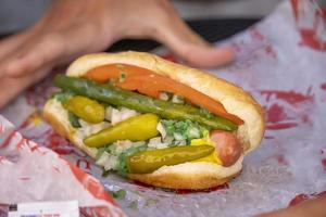 geladen heet hond met augurken pepers, tomaten Aan een bun foto