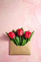 rode tulp bloemen in papieren envelop op gestructureerde roze achtergrond foto
