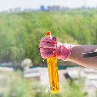 schoonmaakster sprays vloeistof van verstuiven fles naar glas foto