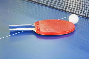 rood peddelen, tennis bal Aan blauw ping pong tafel foto