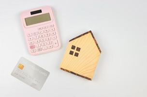 vlak lay-out van houten huis model- , roze rekenmachine en credit kaart Aan wit achtergrond met kopiëren ruimte. huis aankoop concept. foto