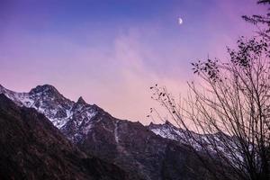 schemering hemel met maan stijgt boven besneeuwde bergen foto