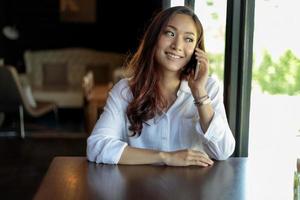jonge Aziatische vrouw in coffeeshop op telefoon foto