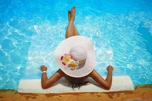 vrouw in witte hoed loungen in het zwembad foto