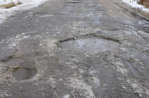beschadigd asfalt weg met kuilen veroorzaakt door bevriezing en ontdooien cycli gedurende de winter. arm weg foto