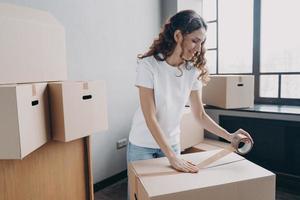 vrouw pakketten dingen in karton doos gebruik makend van kanaal plakband. levering onderhoud, in beweging bedrijf reclame foto