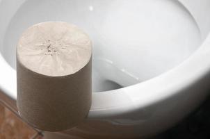 een rollen van grijs toilet papier leugens Aan een wit keramisch toilet in de badkamer foto