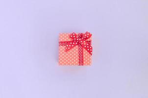 klein rood geschenk doos met lint leugens Aan een paars achtergrond. minimalisme vlak leggen top visie foto