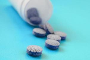 meerdere grijs tablets vallen uit van de plastic pot Aan de blauw oppervlak. achtergrond beeld Aan medisch en farmaceutisch topics foto