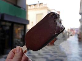 dichtbij omhoog een hand- Holding ijslolly ijs room stok chocola smaak in hand, wazig achtergrond van oud stad- foto