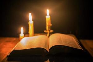 licht kaars met heilig Bijbel en kruis of kruisbeeld Aan oud houten achtergrond in kerk.kaarslicht en Open boek Aan wijnoogst hout tafel Christendom studie en lezing in home.concept van Christus religie foto