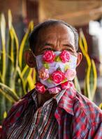 een nep roos met een masker versleten Aan een ouderen gezicht. foto