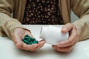 Aziatische oudere vrouw die pil-medicijn in de hand houdt, sterk gezond medisch concept.