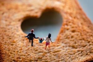liefde concept. miniatuur van gelukkig familie wandelen Aan verbrand gesneden geroosterd brood met een vorm van hart foto