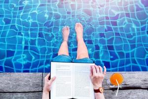 vrouw lezing boek Bij de zwemmen zwembad kant, ontspannende met zomer drinken in haar vakantie, top visie foto