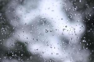 een foto van regen druppels Aan de venster glas met een wazig visie van de bloeiende groen bomen. abstract beeld tonen bewolkt en regenachtig weer voorwaarden