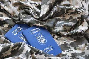 sumie, Oekraïne - maart 20, 2022 oekraïens buitenlands paspoort Aan kleding stof met structuur van leger korrelig camouflage. kleding met camo patroon in grijs, bruin en groen pixel vormen en oekraïens ID kaart foto