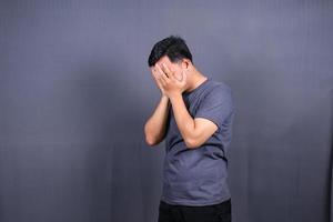 depressief Aziatisch jong Mens hebben stressvol tijd met handen aan het bedekken gezicht. geïsoleerd Aan grijs achtergrond. foto