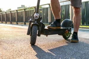 dichtbij omhoog voeten van een Mens in sportschoenen gemaakt hou op staan een been Aan elektrisch scooter hebben een rijden Aan de straten of park na werk buitenshuis. selectief focus Aan voeten. foto