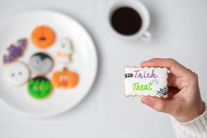 vrouw hand met grappige halloween cookie tijdens het drinken van koffie. fijne halloween-dag, truc of bedreiging, hallo oktober, herfstherfst, traditioneel, feest- en vakantieconcept foto