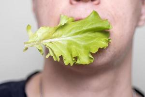 een Mens houdt een vers groen sla blad in zijn mond. gezond levensstijl. foto