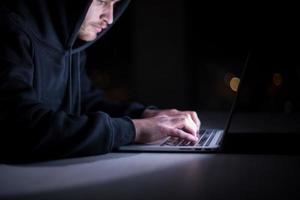 hacker gebruik makend van laptop computer terwijl werken in donker kantoor foto