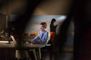 Mens werken Aan computer in donker kantoor foto