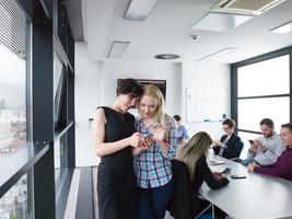 twee elegant Dames gebruik makend van mobiel telefoon door venster in kantoor gebouw foto