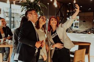 groep van vrolijk collega's nemen selfie en gebaren terwijl staand in de modern kantoor. foto