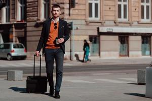 gaan naar luchthaven terminal. zelfverzekerd zakenman reiziger wandelen Aan stad straten en trekken zijn koffer drinken koffie en sprekend Aan smartphone foto