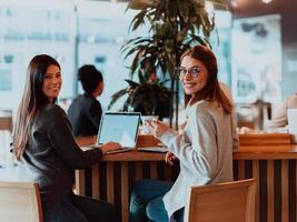 twee jong bedrijf Dames zittend Bij tafel in cafe. meisje shows collega informatie Aan laptop scherm. meisje gebruik makend van smartphone, bloggen. teamwerk, bedrijf ontmoeting.. foto