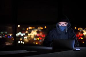 hacker gebruik makend van laptop computer terwijl werken in donker kantoor foto