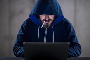 jong hacker gebruik makend van laptop computer terwijl werken in donker kantoor foto