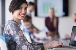 jong bedrijf vrouw Bij kantoor werken Aan laptop met team Aan vergadering in achtergrond foto