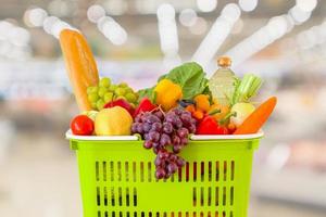 winkelmandje gevuld met groenten en fruit met supermarkt supermarkt wazig onscherpe achtergrond met bokeh licht foto