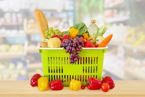 winkelmandje gevuld met fruit en groenten op houten tafel met supermarkt supermarkt wazig onscherpe achtergrond met bokeh licht foto