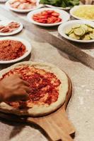 persoon die toppings op pizza zet foto