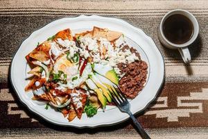 chilaquiles Mexicaans voedsel met in rood saus, kaas, room, Chili paprika's Aan wijnoogst achtergrond en koffie foto