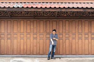 Aziatisch lang haar- Mens is staand en posten in voorkant van klassiek backdrop hout muur en deur in voorkant van Thailand wijnoogst traditioneel gebouw. foto