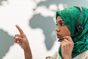 afro moslim vrouw met groen hijab sjaal klant vertegenwoordiger bedrijf vrouw met telefoon koptelefoon helpen en ondersteunen online met klant in modern telefoontje centrum foto