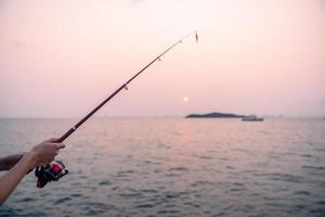 vrouw hand- Holding visvangst hengel met zee achtergrond, visvangst Bij zonsondergang. foto