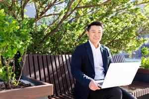 vrolijk Aziatisch Mens op zoek Bij camera en glimlachen zakenman werken Aan laptop foto