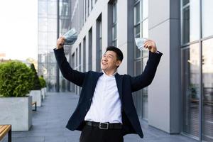 mannetje Aziatisch zakenman verheugt zich Holding een veel van contant geld dollars kreeg een groot winnen en uitbetaling foto