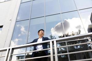 Aziatisch zakenman baas staat in de buurt zijn kantoor centrum Aan de balkon in een donker kleur bedrijf pak foto