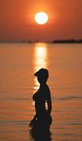 zonsondergang oceaan visie. zon bovenstaand de zee Aan oranje lucht. vrouw staand Aan strand. foto