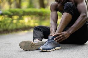 Afrikaanse sportman loper Mens zittend Aan jogging bijhouden gebruik makend van hand- Holding enkel en gevoel pijn in zijn enkel, kopiëren ruimte. sport- letsel concept foto