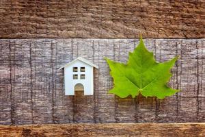 speelgoedhuis en groen esdoornblad op houten achtergrond foto