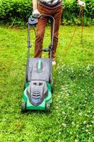 man die groen gras snijdt met grasmaaier in de achtertuin. tuinieren land levensstijl achtergrond. prachtig uitzicht op vers groen grasgazon in zonlicht, tuinlandschap in lente- of zomerseizoen. foto